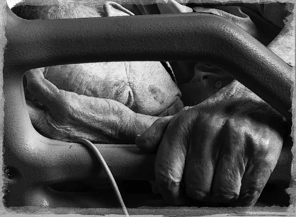 Black and white photograph of two pairs of hands resting on the arms of a hospital chair, divided horizontally by the armrest.