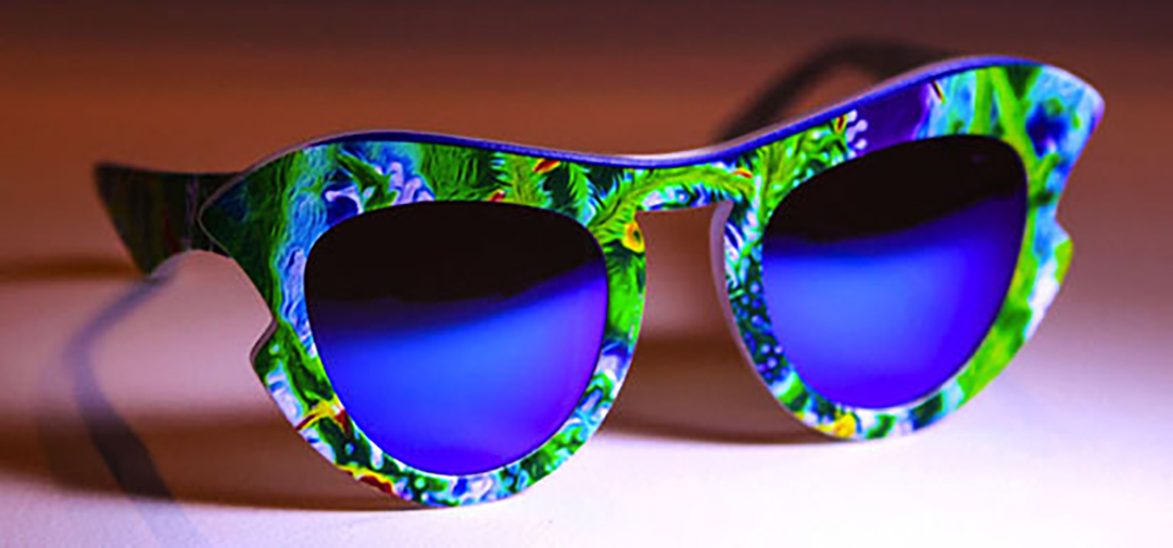 Cat-eye eyewear frames printed with a green, blue and yellow abstract foliage pattern with blue mirrored lenses.