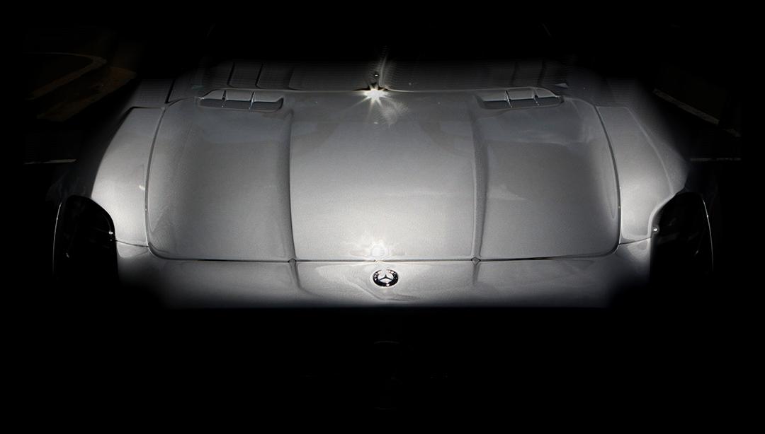 Low-key digital photographic painting of the silver hood and nose of a Mercedes SLS emerging from darkness, lit along the centre ridge.