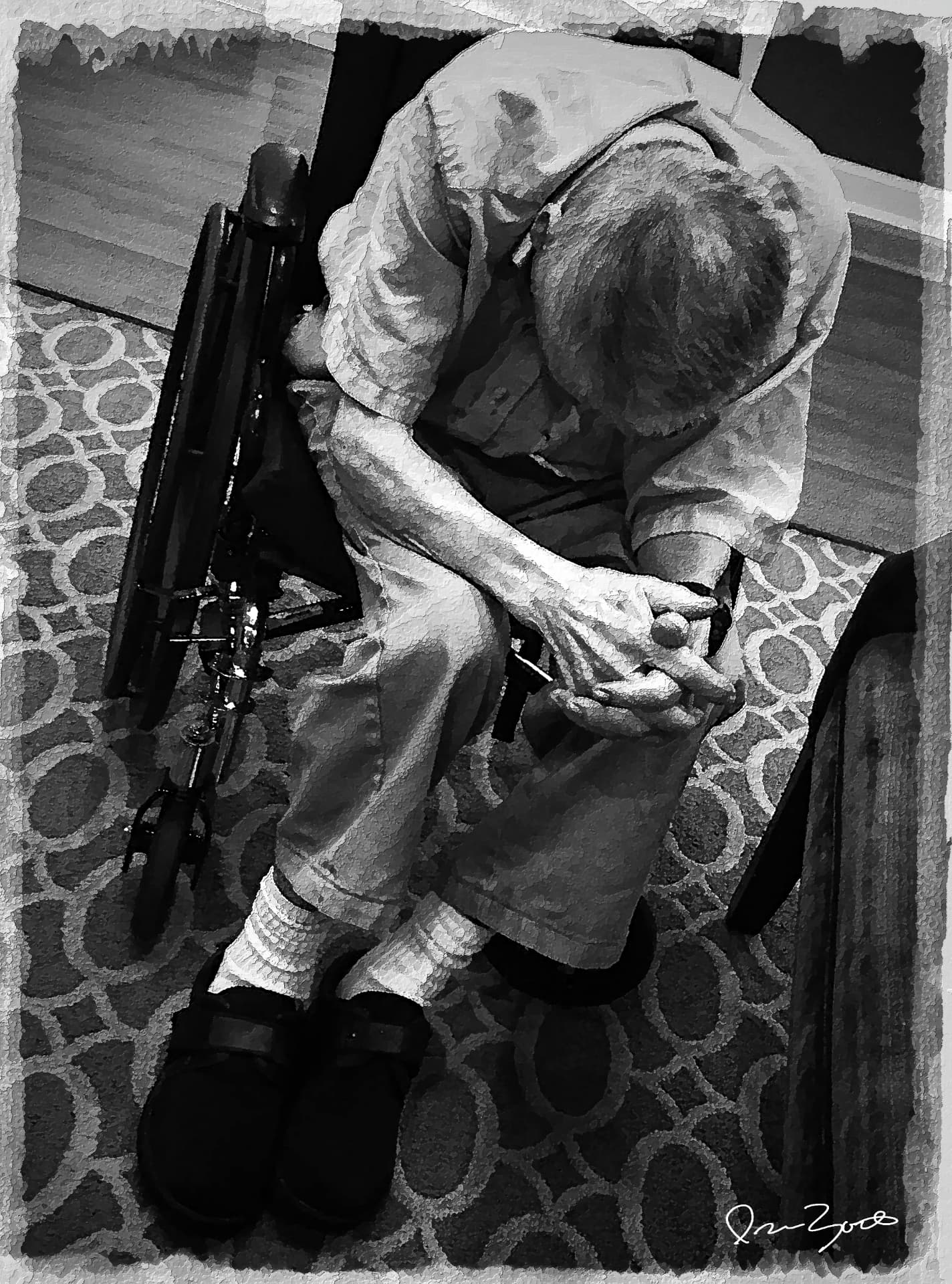 Black and white overhead photograph of an elderly man seated with clasped hands, a folded wheelchair beside him on a patterned circle rug.