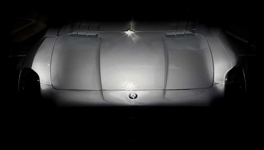 Low-key digital photographic painting of the silver hood and nose of a Mercedes SLS emerging from darkness, lit along the centre ridge.